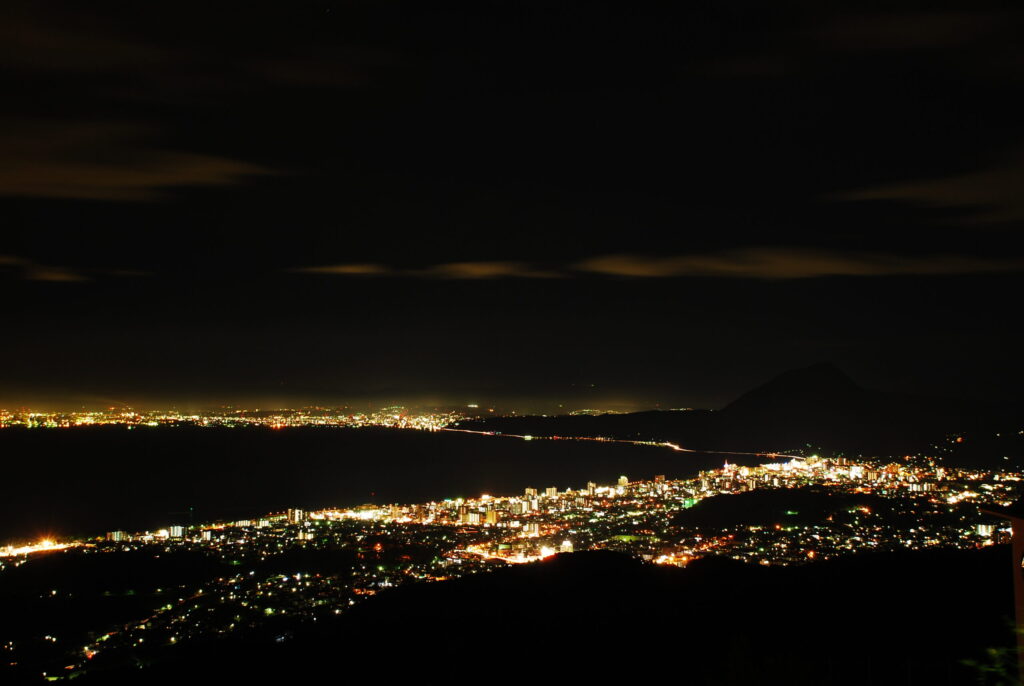 Stunning city lights of Beppu Onsen town shining at night, viewed from Jumonjibaru Observatory - Japan Navi Journey