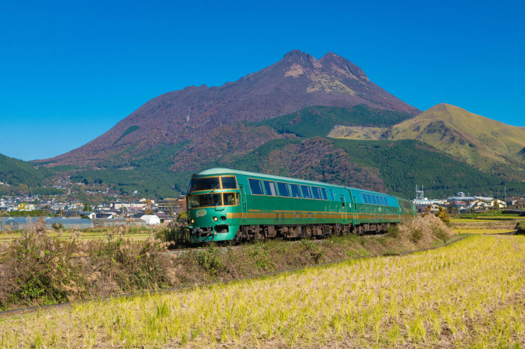The green Yufuin no Mori sightseeing train running with Mount Yufu in the background - Tailor-Made Japan Experience with Japan Navi Journey